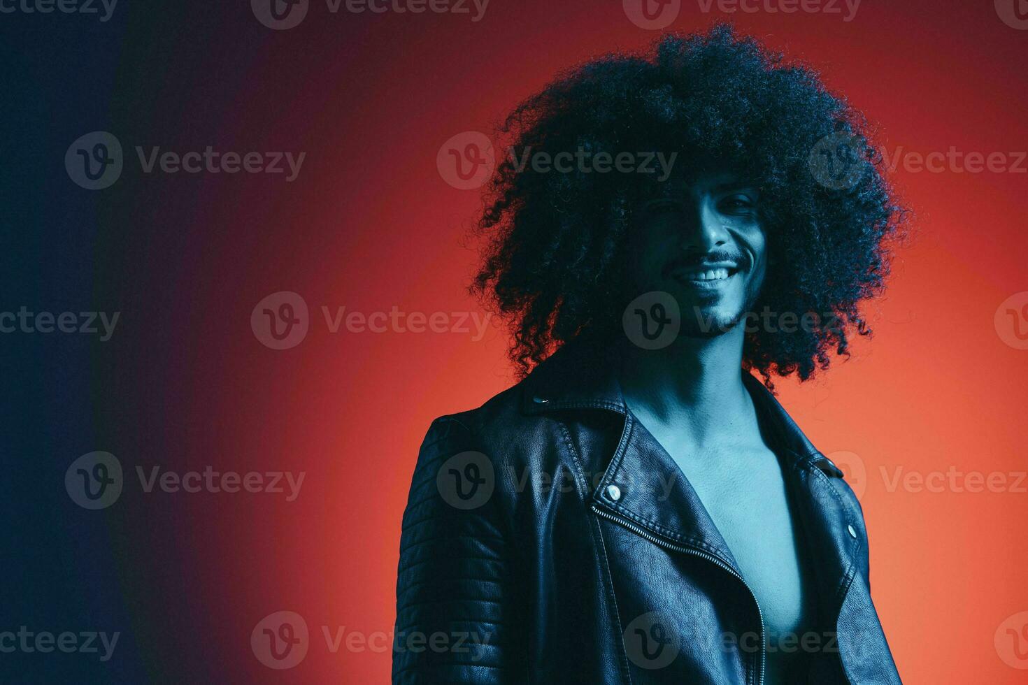 Portrait of fashion man with curly hair on red background multinational, colored light, black leather jacket trend, modern concept. photo