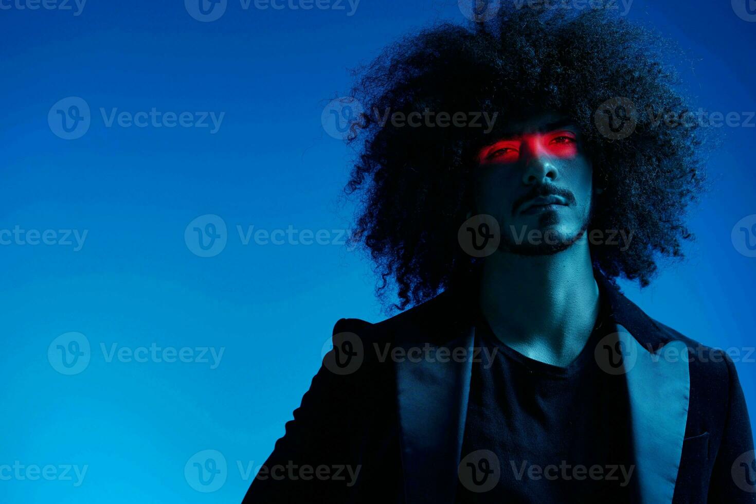 Fashion portrait of a man with curly hair on a blue background with a red stripe of light, multicolored light, trendy, modern concept. photo