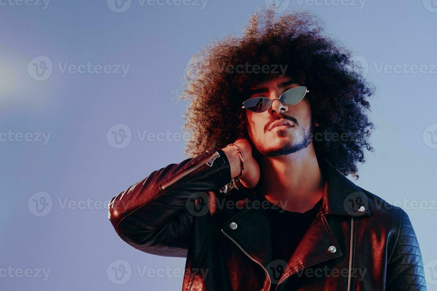 Portrait of a stylish man with curly hair on a blue background multinational, colored light, trendy glasses, modern concept. photo