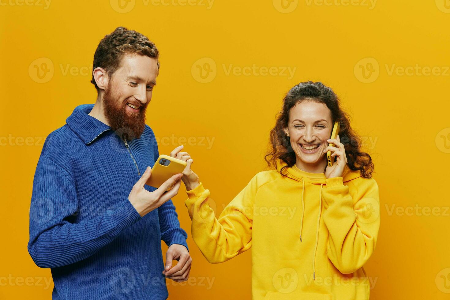 Woman and man cheerful couple with phones in hand talking on cell phone crooked smile cheerful, on yellow background. The concept of real family relationships, talking on the phone, work online. photo