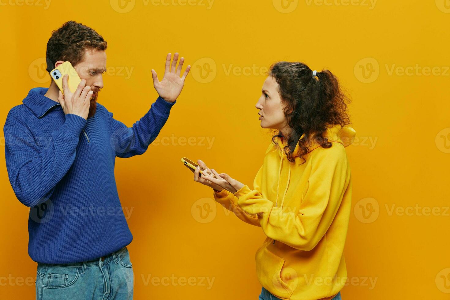 Woman man cheerful couple with phones in hand social networking and communication crooked smile fun and fight, in yellow background. The concept of real family relationships, freelancers, work online. photo