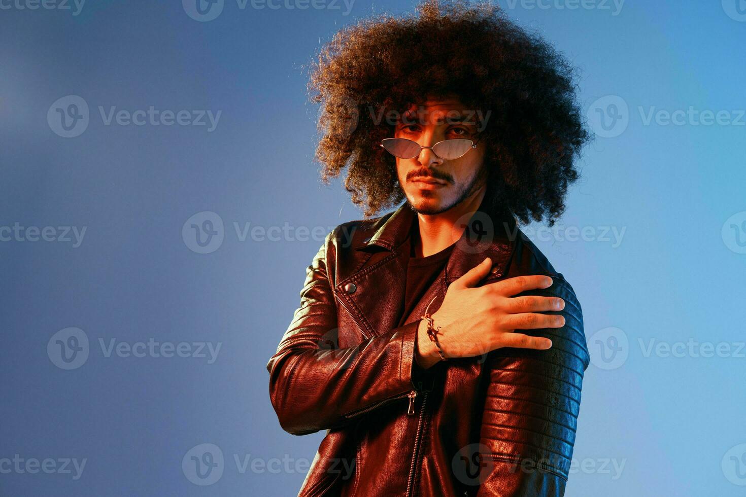 Portrait of a stylish man with curly hair on a blue background multinational, colored light, trendy glasses, modern concept. photo
