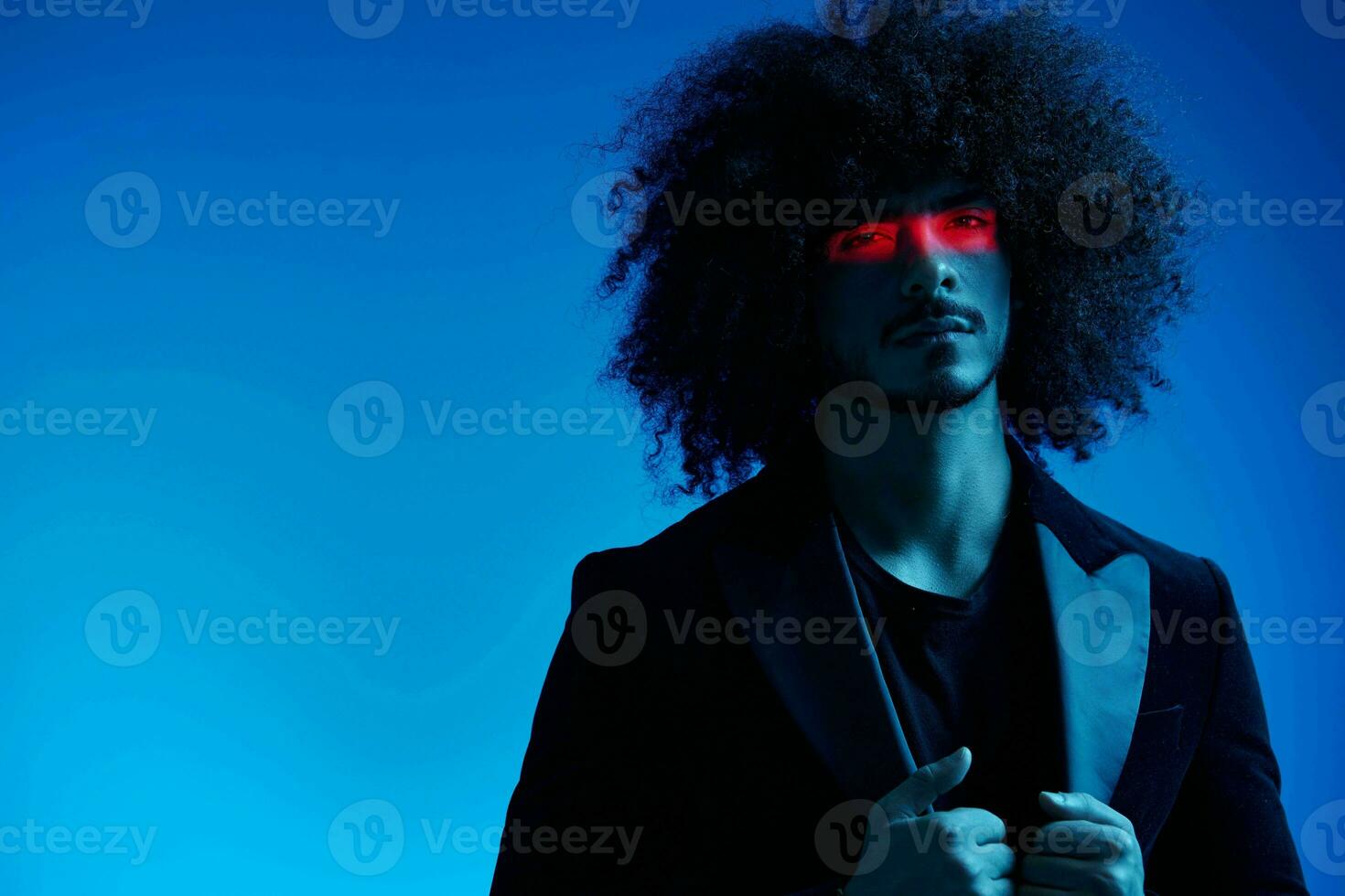 Fashion portrait of a man with curly hair on a blue background with a red stripe of light, multicolored light, trendy, modern concept. photo