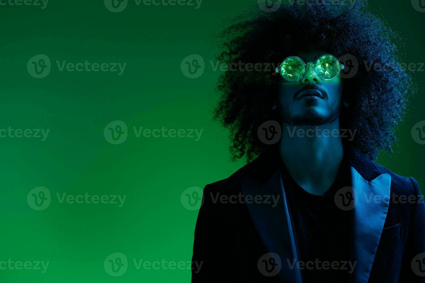 Fashion portrait of a man with curly hair on a green background with sunglasses, multinational, colored pink light, trendy, modern concept. photo