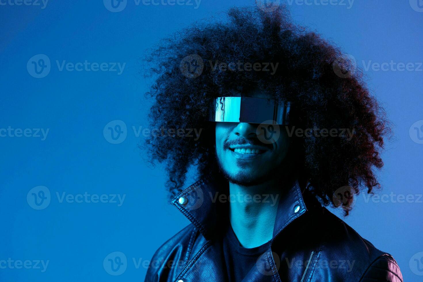 Portrait of fashion man with curly hair with stylish glasses on blue background multinational, colored light, black leather jacket trend, modern concept. photo