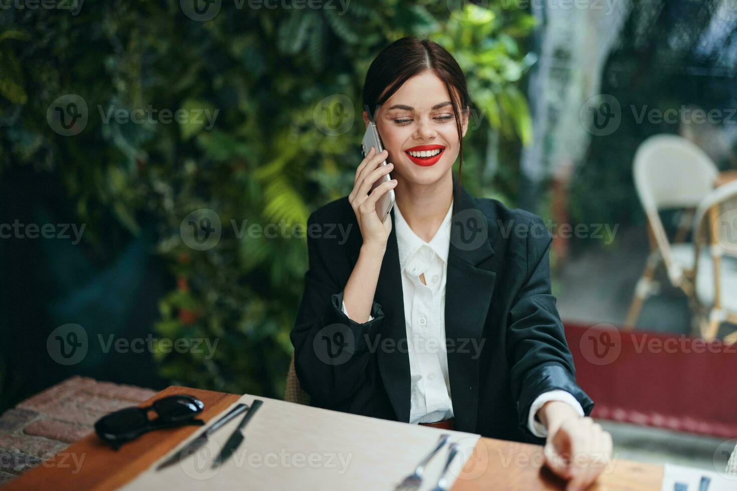 A woman blogger tourist sits in a cafe at a table with a phone in her hands talking on the phone, mobile communications and the Internet on a spring trip, business call, freelance work online, smile photo
