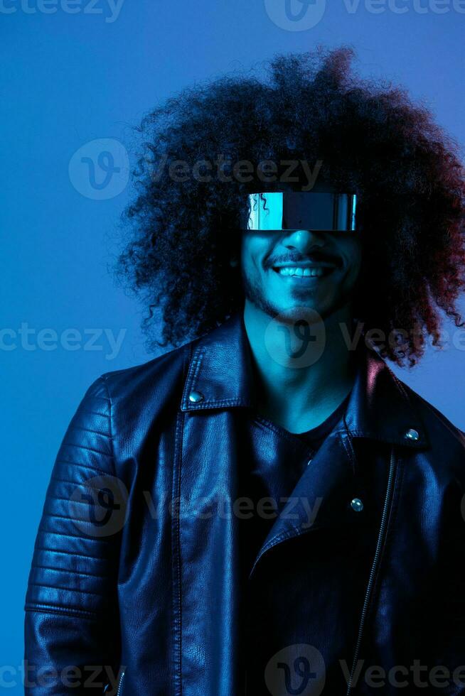 Portrait of fashion man with curly hair with stylish glasses on blue background multinational, colored light, black leather jacket trend, modern concept. photo