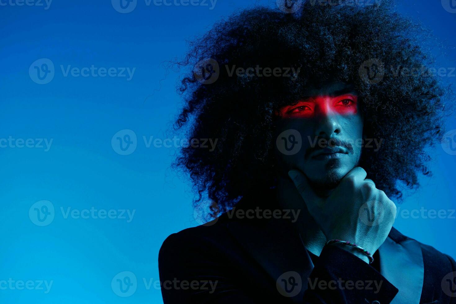 Fashion portrait of a man with curly hair on a blue background with a red stripe of light, multicolored light, trendy, modern concept. photo