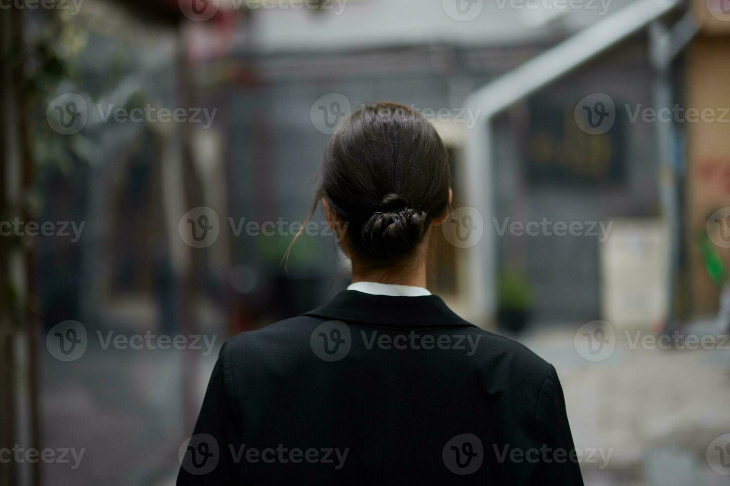 Stylish woman in a black jacket walks along the city street with her back to the camera, follow me photo