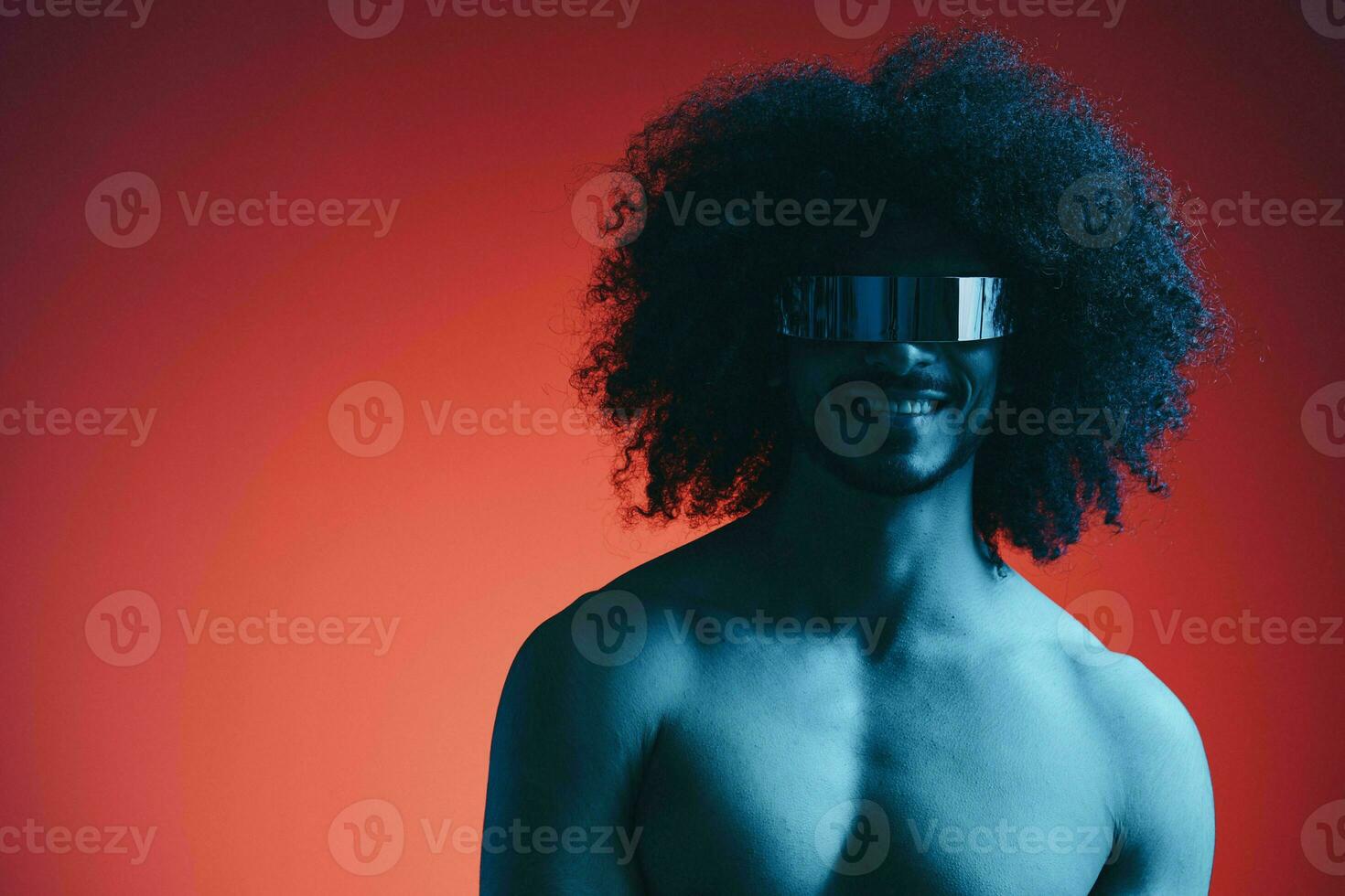 Portrait of fashion man with curly hair on red background with stylish glasses, multinational, colored light, black leather jacket trend, modern concept, sexy body. photo