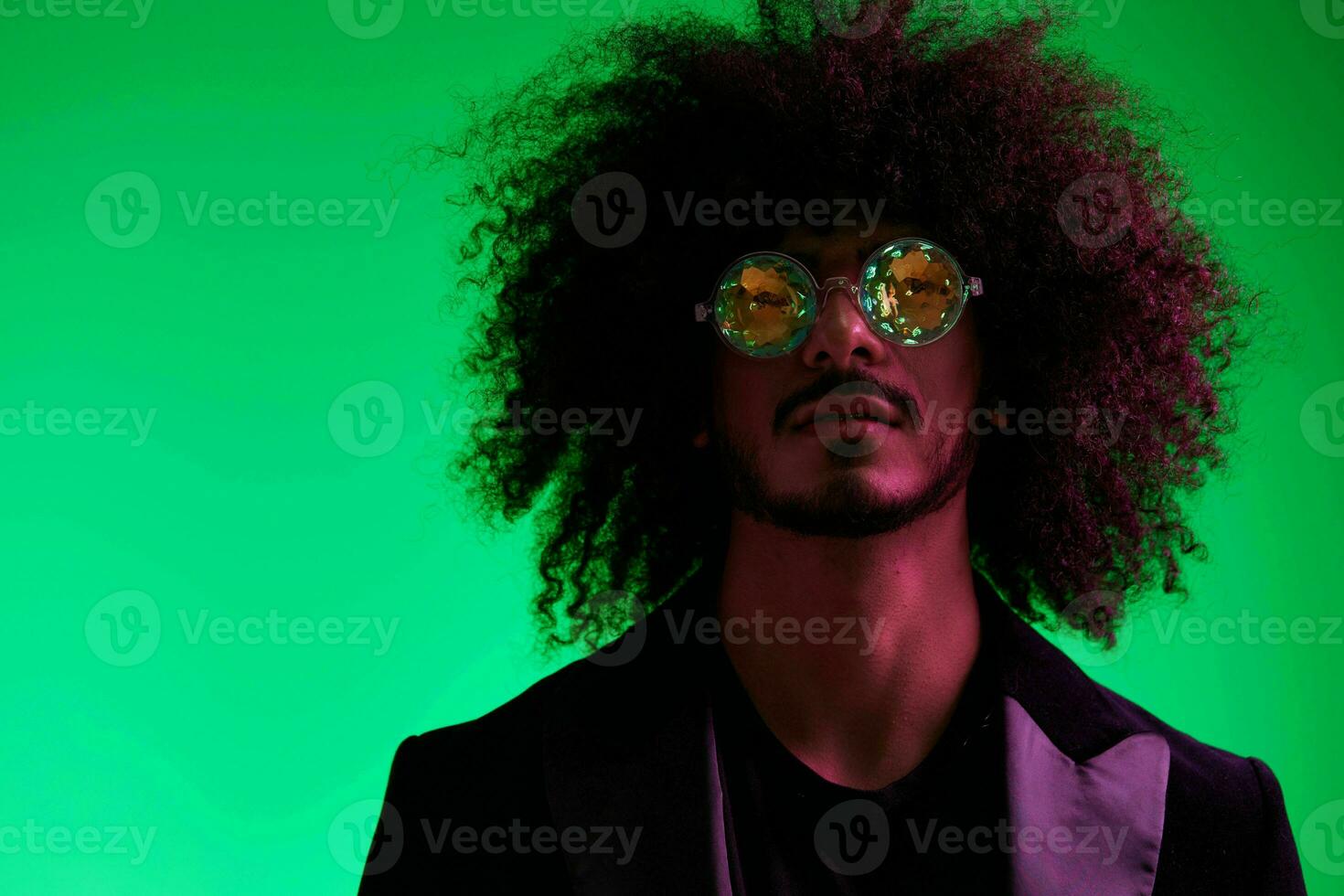 Fashion portrait of a man with curly hair on a green background with sunglasses, multinational, colored pink light, trendy, modern concept. photo