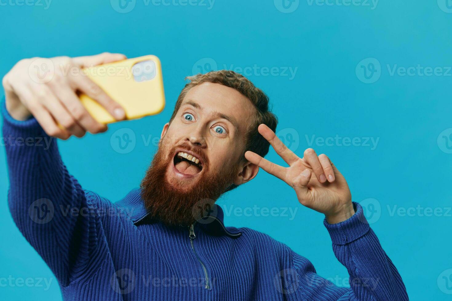 retrato de un hombre con un teléfono en su manos blogger toma autofotos, en un azul antecedentes. comunicado en línea social medios de comunicación, estilo de vida foto