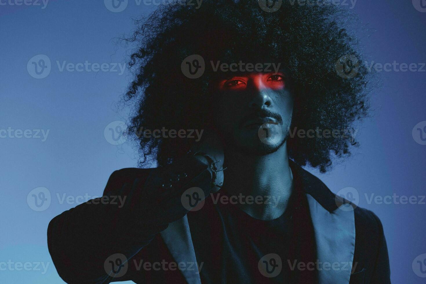 Fashion portrait of a man with curly hair on a blue background with a red stripe of light, multicolored light, trendy, modern concept. photo