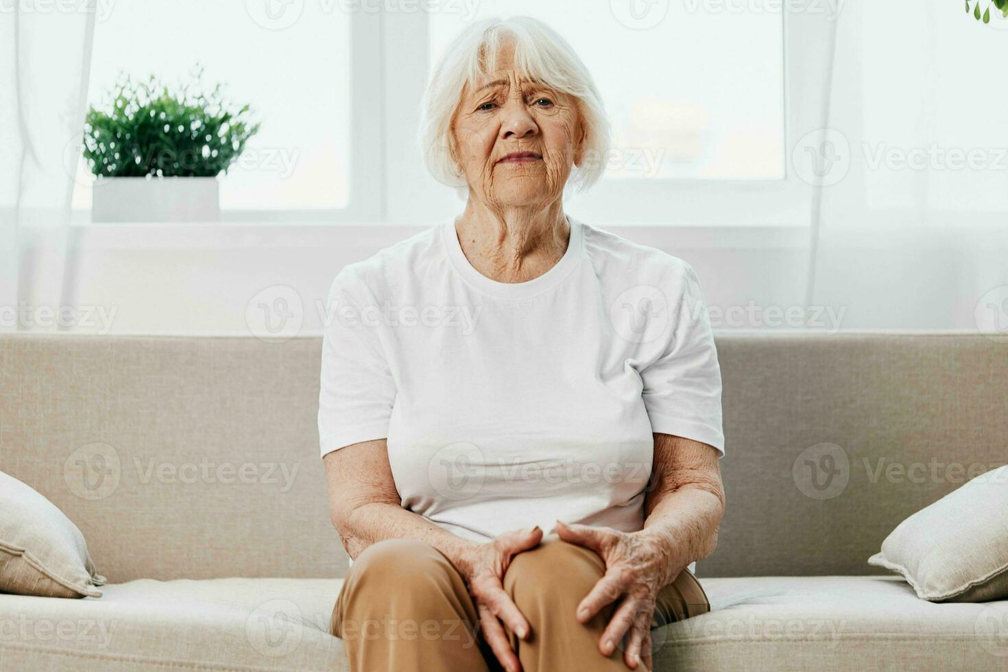 mayor mujer grave dolor en su pierna sentado en el sofá, salud problemas en antiguo edad, pobre calidad de vida. abuela con gris pelo sostiene en a su dolorido rodilla, problemas con articulaciones y ligamentos foto