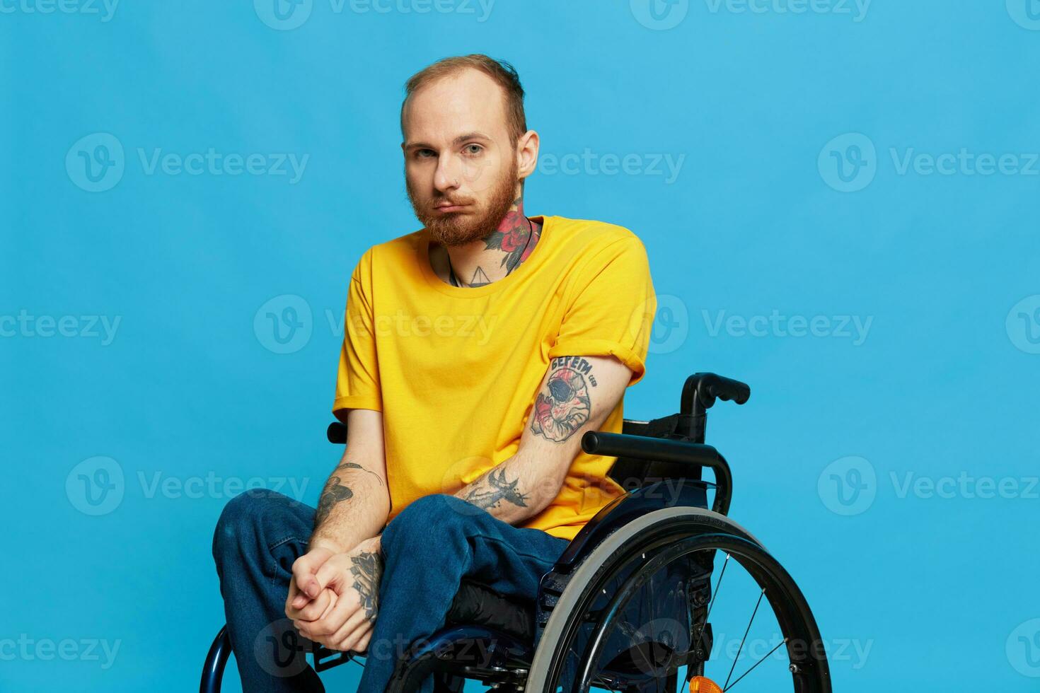 a man sits in a wheelchair in a t-shirt on a blue background in the studio, the concept of a free barrier-free environment for people with disabilities photo