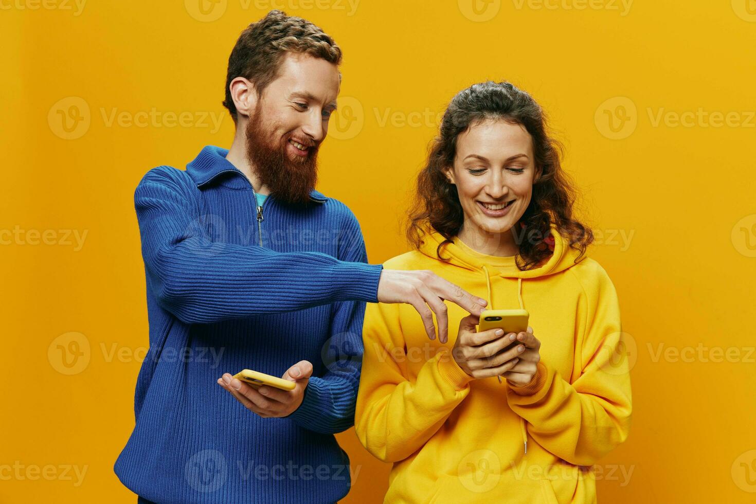 Woman man cheerful couple with phones in hand social networking and communication crooked smile fun and fight, in yellow background. The concept of real family relationships, freelancers, work online. photo