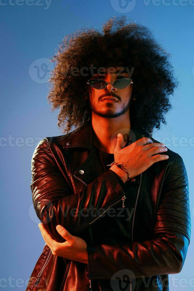 Portrait of a stylish man with curly hair on a blue background multinational, colored light, trendy glasses, modern concept. photo