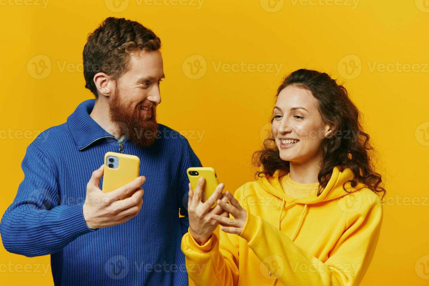 Man and woman couple smiling merrily with phone in hand social media viewing photos and videos, on yellow background, symbols signs and hand gestures, family freelancers.