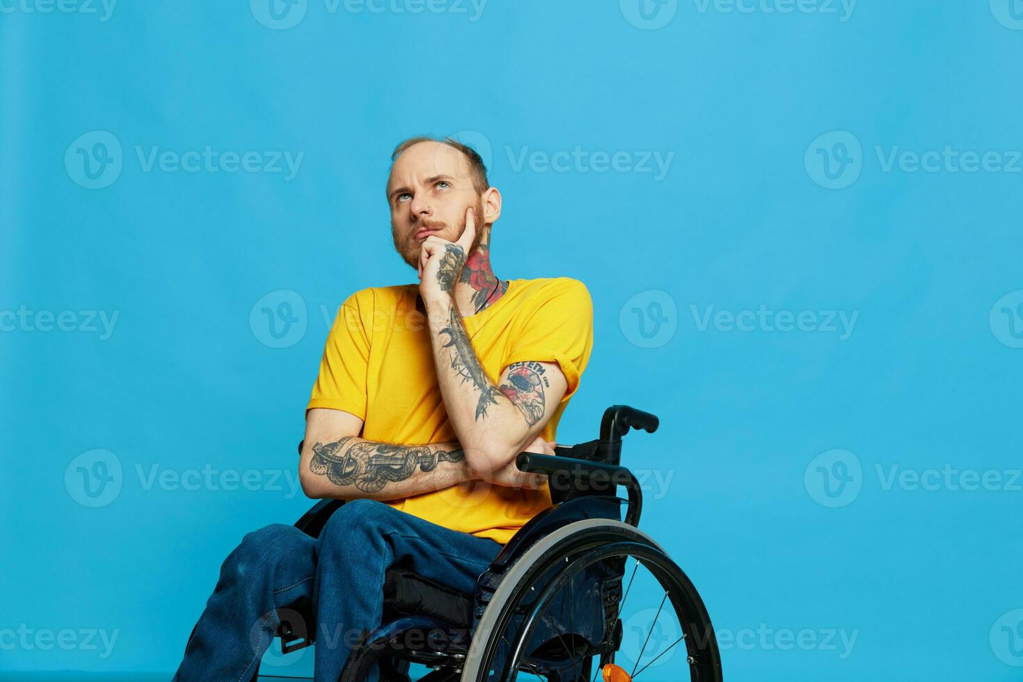 a man sits in a wheelchair thoughtfulness in a t-shirt on a blue background in the studio, the concept of a free barrier-free environment for people with disabilities photo