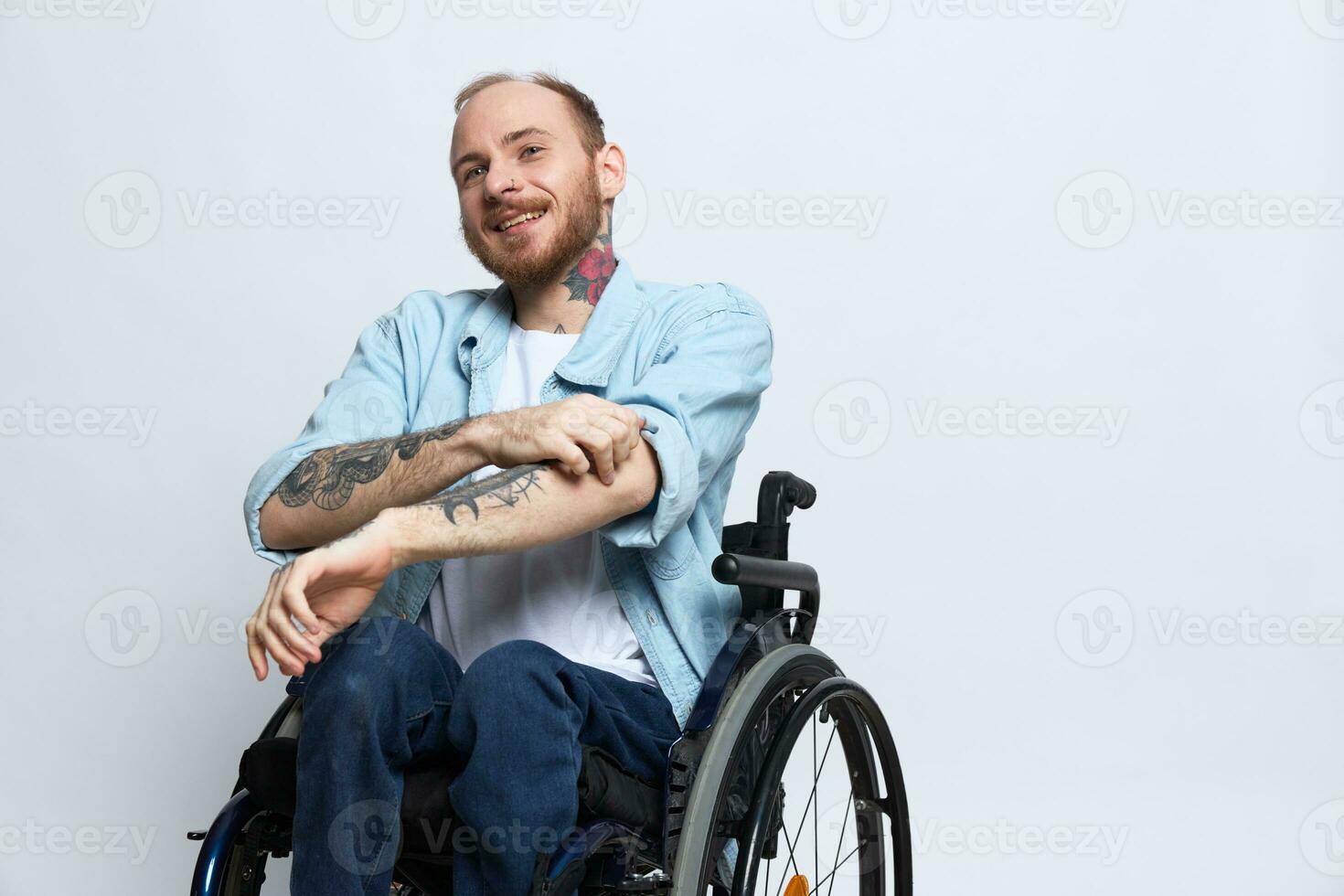 A man in a wheelchair smile, copy space, with tattoos on his arms sits on a gray studio background, the concept of health is a person with disabilities, a real person photo