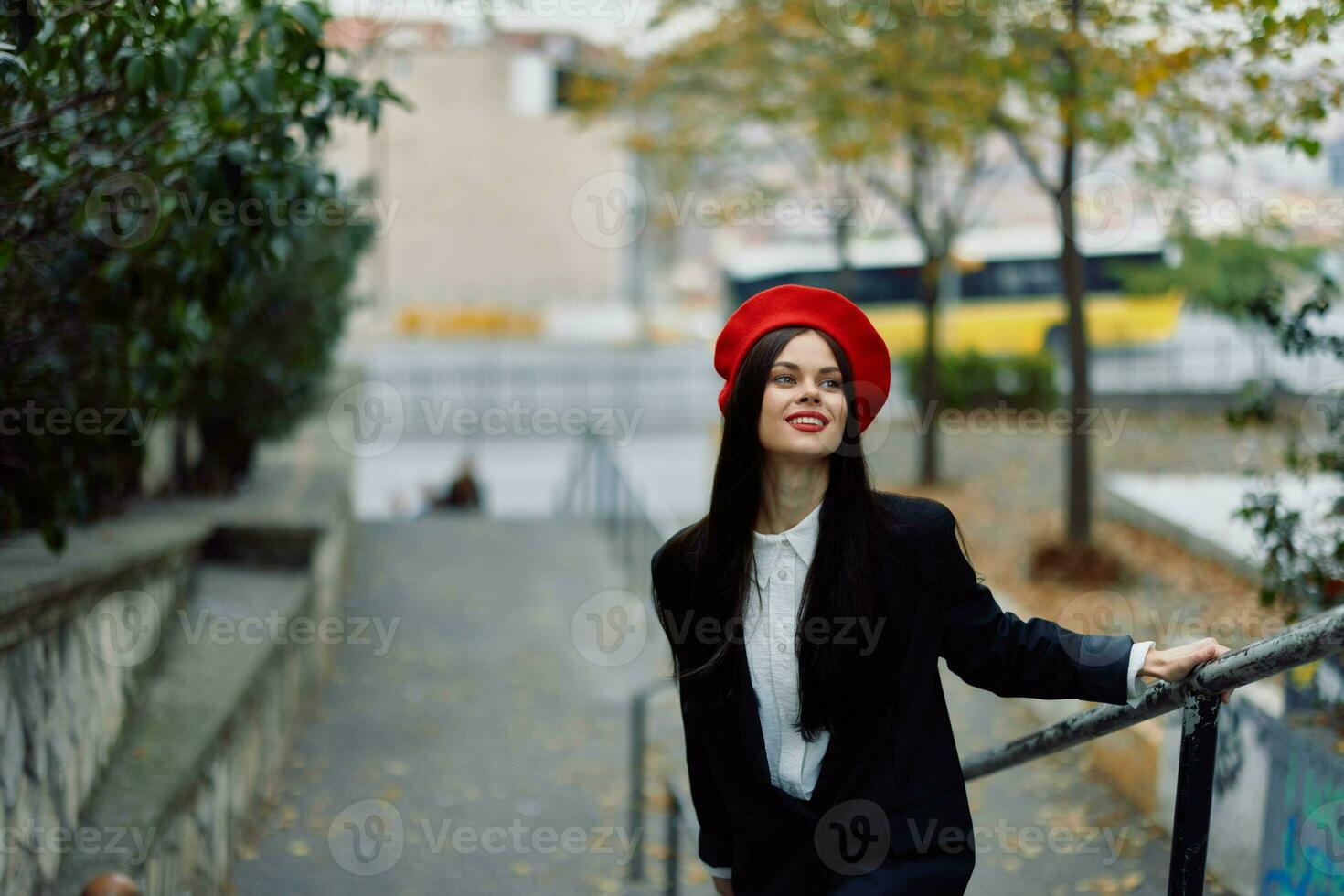 Moda mujer caminando abajo pasos en contra ciudad fondo en elegante ropa con rojo labios y rojo boina, viajar, cinematográfico color, retro Clásico estilo, urbano Moda estilo de vida. foto