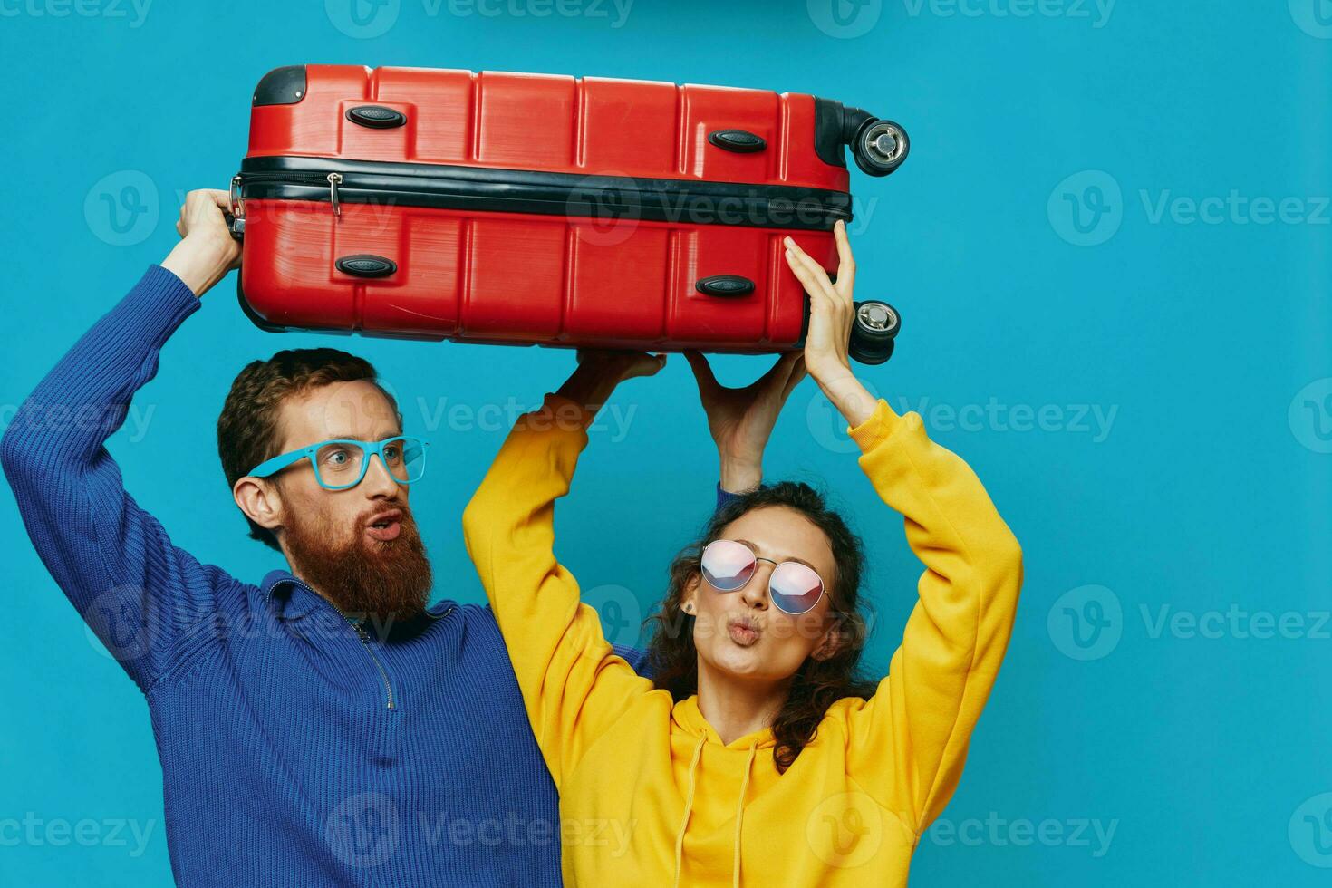 Woman and man smile suitcases in hand with yellow and red suitcase smile fun, on blue background, packing for a trip, family vacation trip. photo