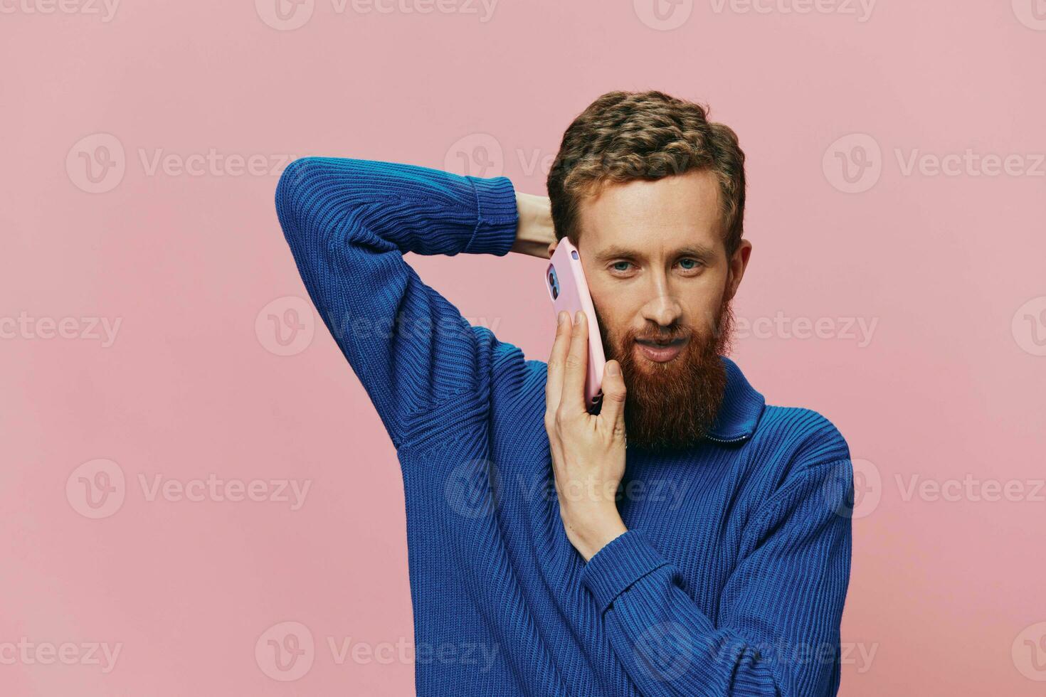 Portrait of a man with a phone in his hands doing looking at it and talking on the phone, on a pink background. Communicating online social media, lifestyle photo