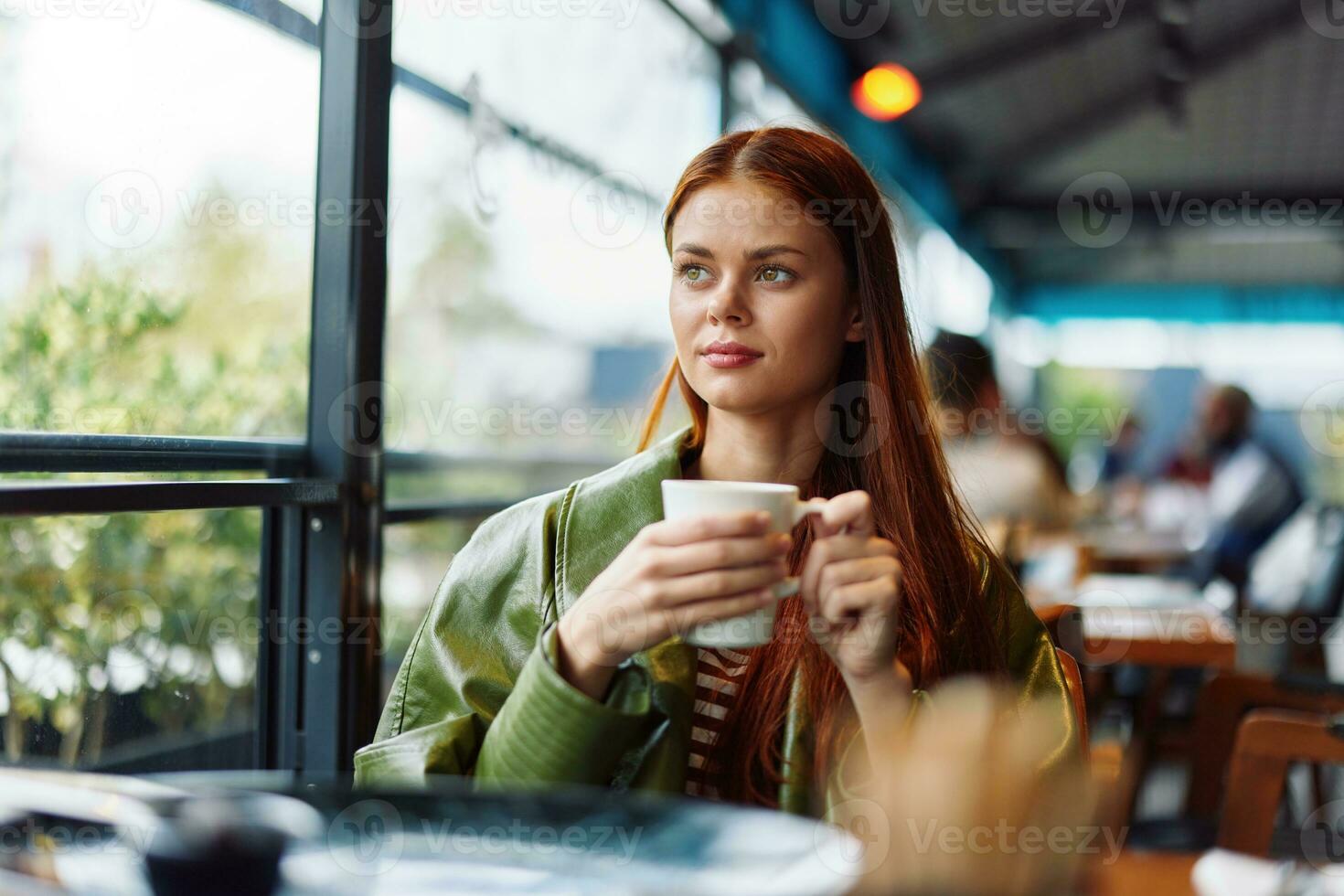 Stylish Influencer woman drinking a drink from a mug in a cafe and smiling looking out the window, content blogger photo