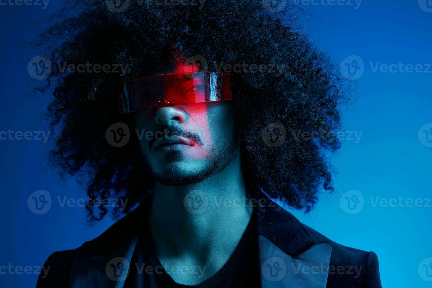 Fashion portrait of a man with curly hair on a blue background wearing red sunglasses, multinational, colored light, trendy, modern concept. photo