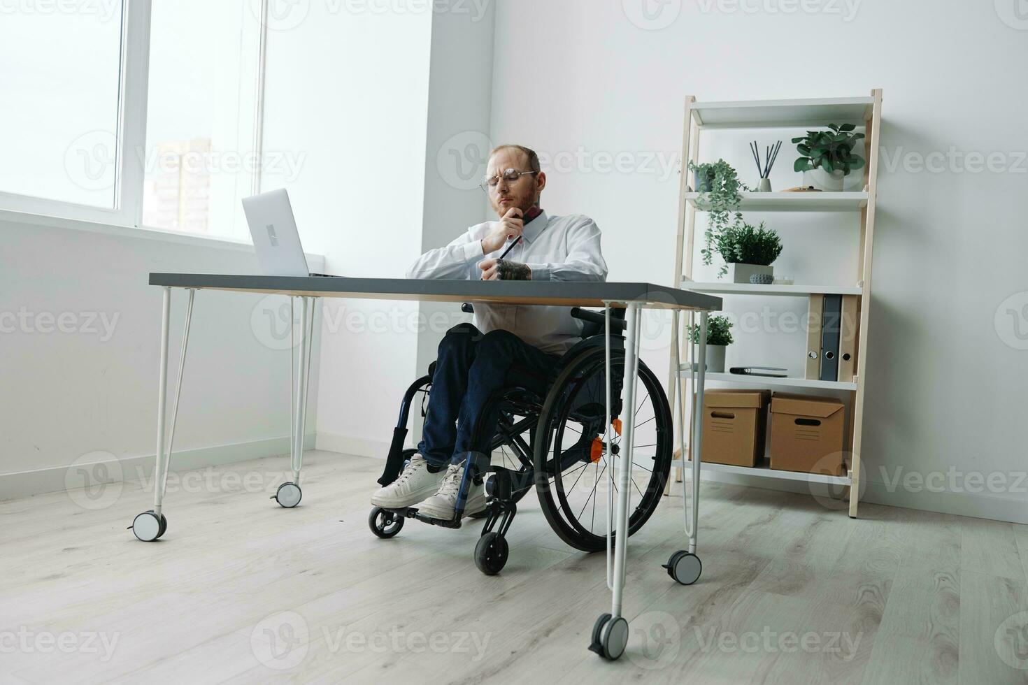 A man in a wheelchair, a businessman in the office works at a laptop, writing down a plan in a notebook, thoughtfulness, integration into society, the concept of working a person with disabilities photo