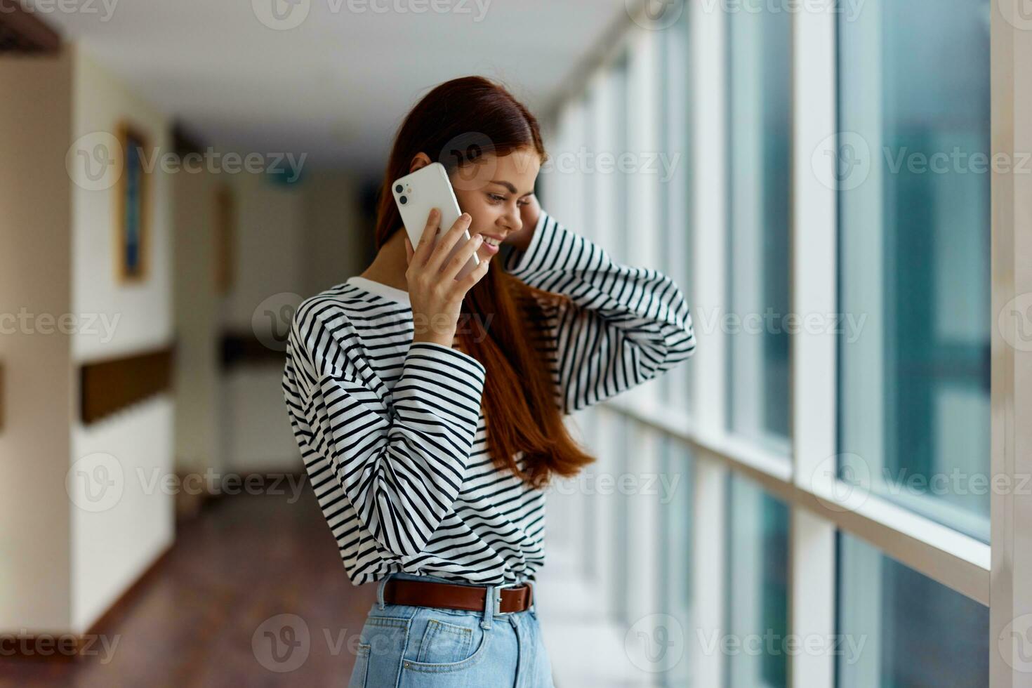 A woman with a phone in her hands talking and laughing while looking out the window at the city photo