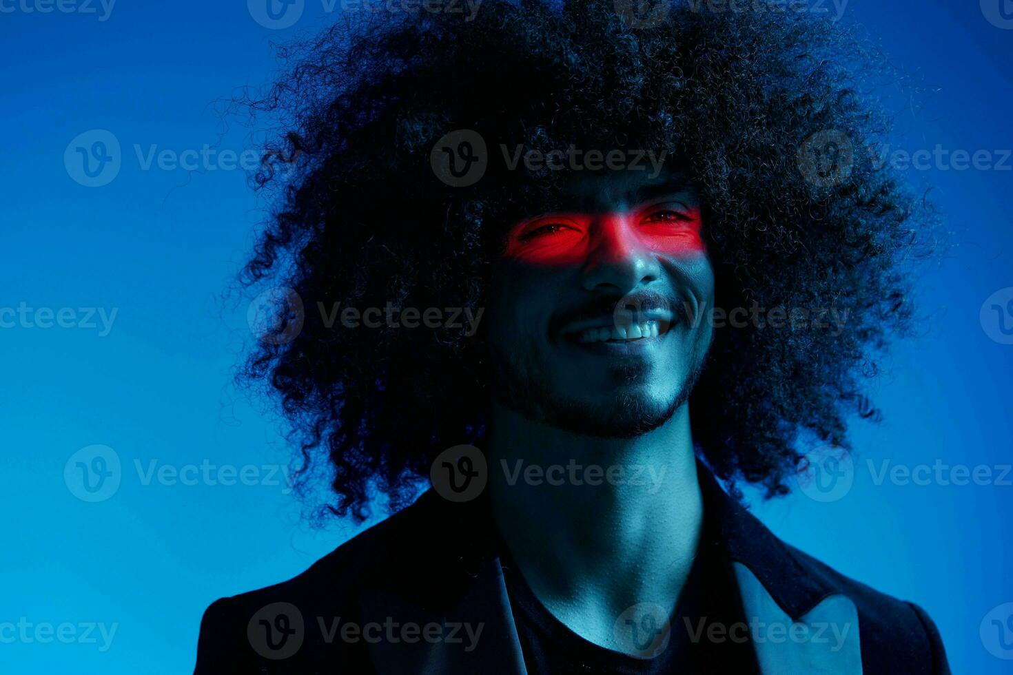 Fashion portrait of a man with curly hair on a blue background with a red stripe of light, multicolored light, trendy, modern concept. photo