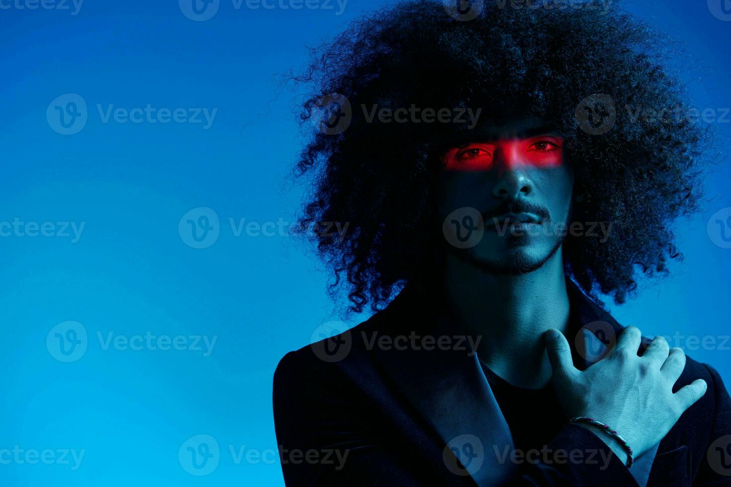 Fashion portrait of a man with curly hair on a blue background with a red stripe of light, multicolored light, trendy, modern concept. photo