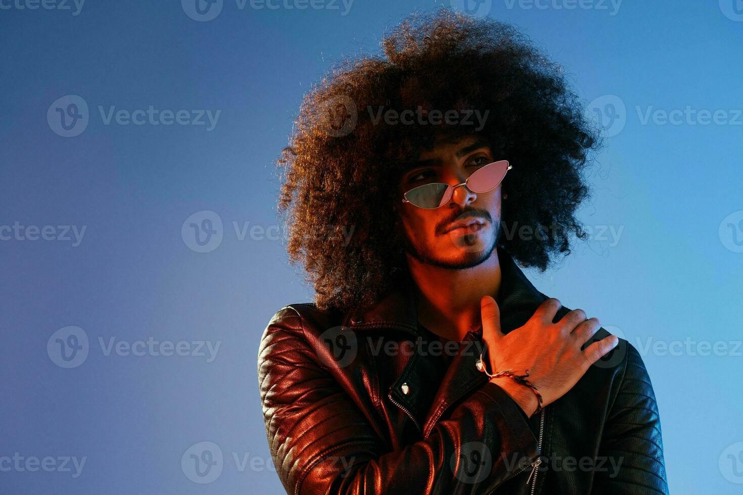 Portrait of a stylish man with curly hair on a blue background multinational, colored light, trendy glasses, modern concept. photo