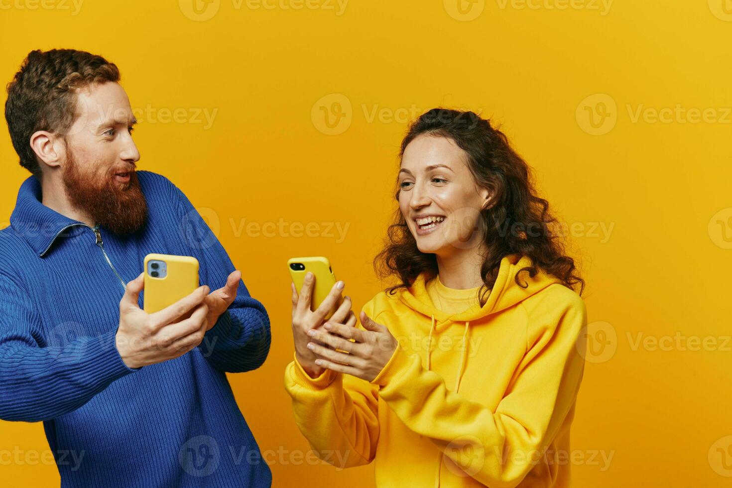 Man and woman couple smiling merrily with phone in hand social media viewing photos and videos, on yellow background, symbols signs and hand gestures, family freelancers.