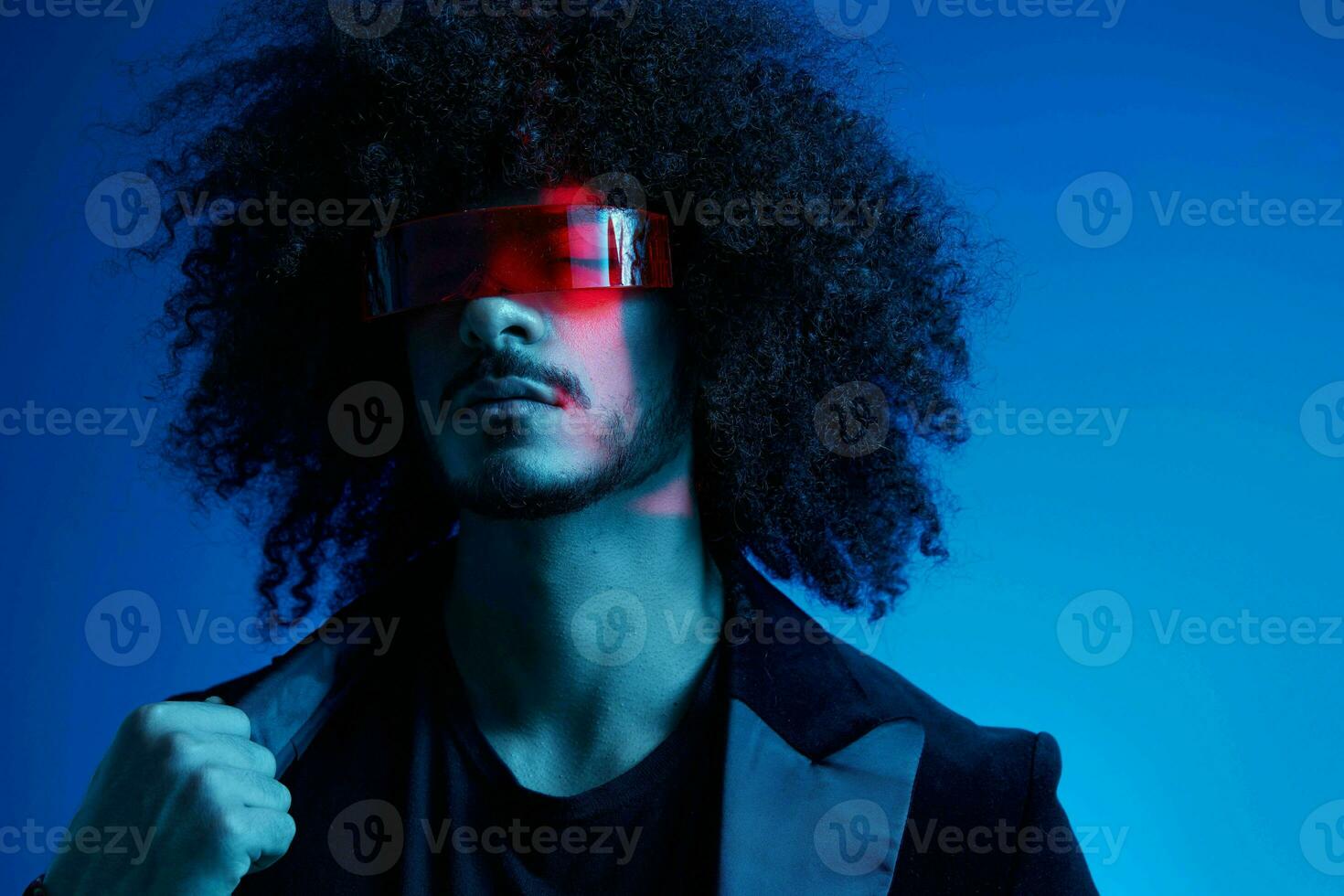 Fashion portrait of a man with curly hair on a blue background wearing red sunglasses, multinational, colored light, trendy, modern concept. photo