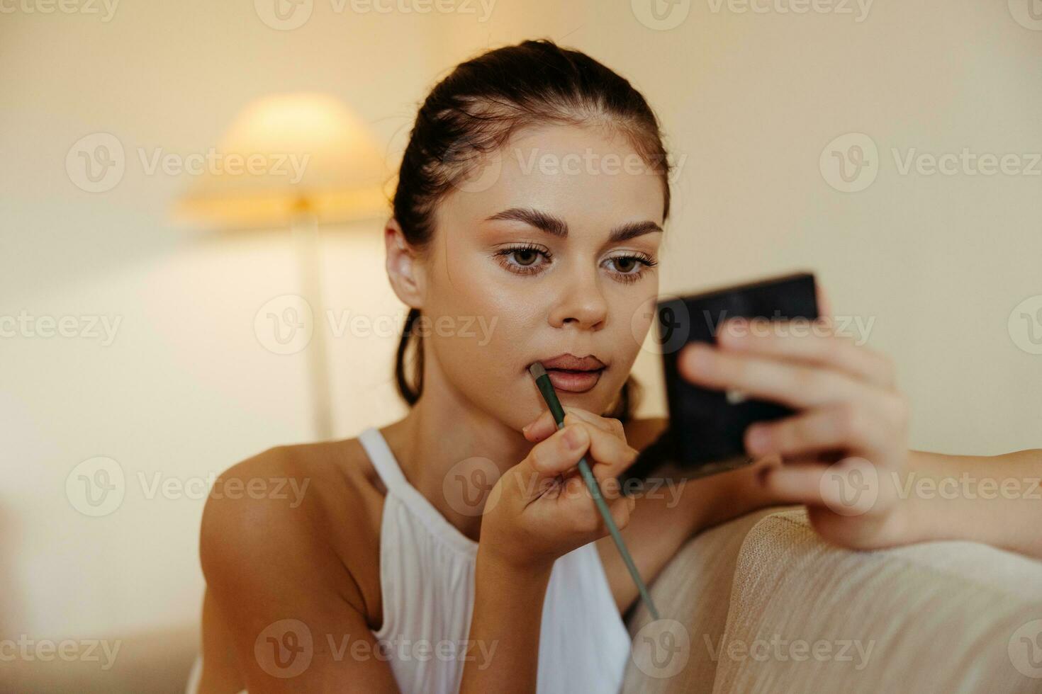 A woman at home looks in the mirror and applies makeup lipstick, beauty concept, problem skin care with acne, home makeup. photo