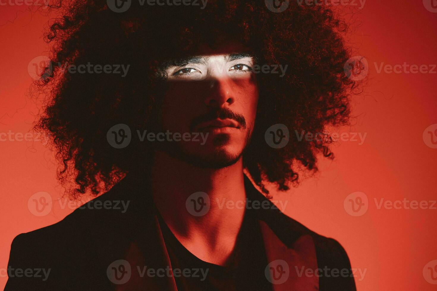 Fashion portrait of a man with curly hair on a red background, multinational, colored light, trendy, modern concept. photo