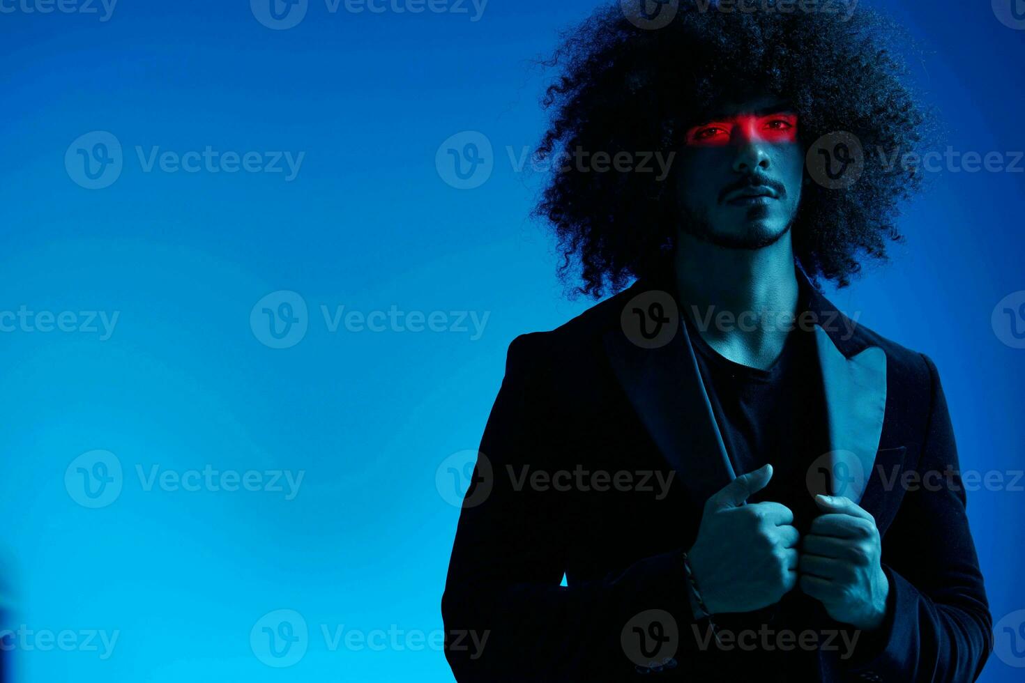 Fashion portrait of a man with curly hair on a blue background with a red stripe of light, multicolored light, trendy, modern concept. photo