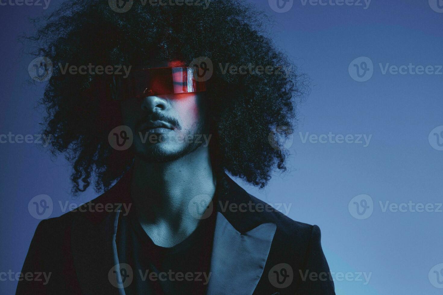 Fashion portrait of a man with curly hair on a blue background wearing red sunglasses, multinational, colored light, trendy, modern concept. photo