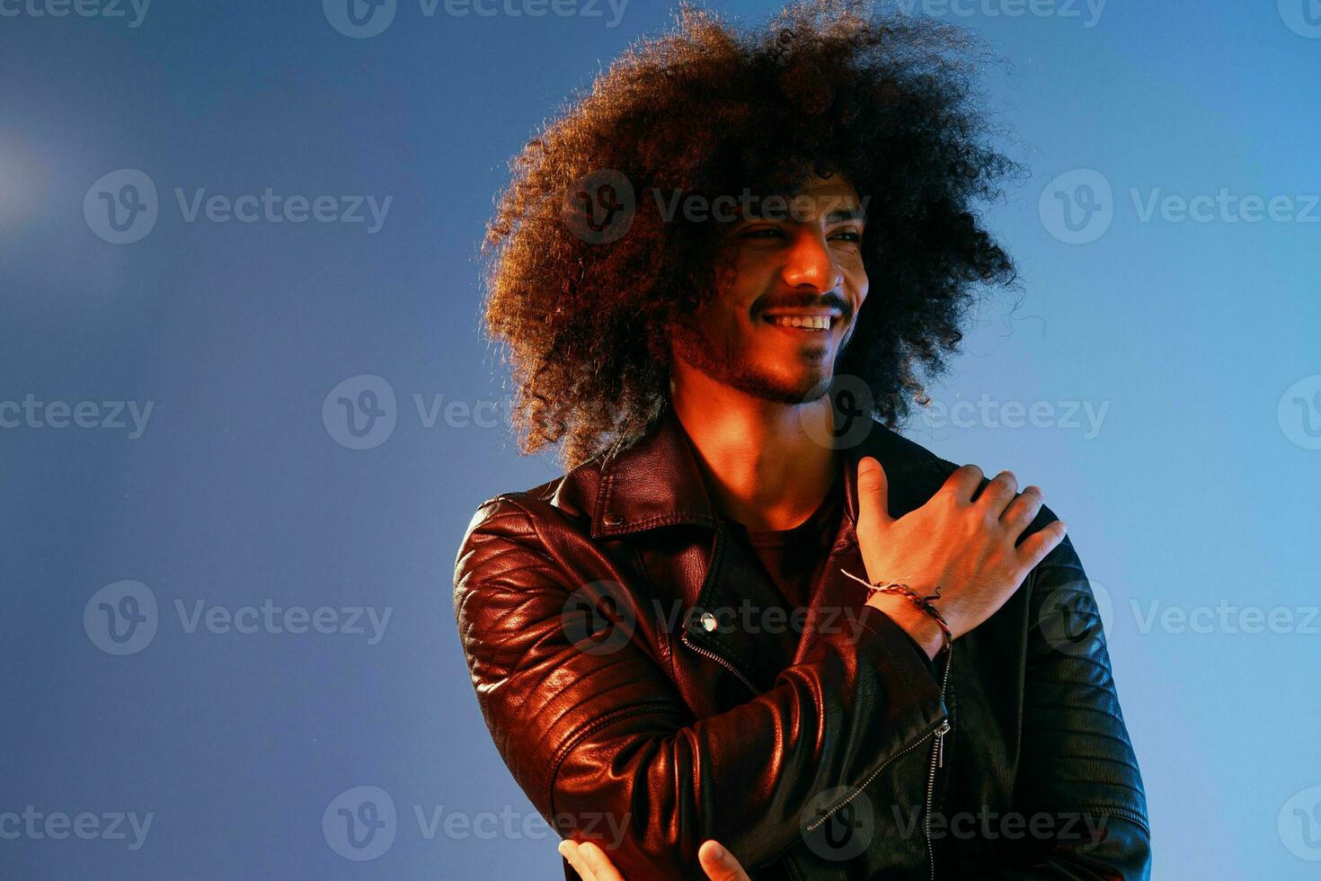 Portrait of a stylish man with curly hair on a blue background multinational, colored light, black leather jacket trend, modern concept. photo