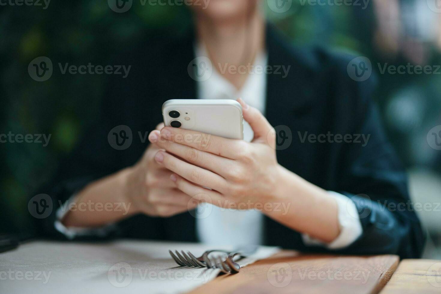 un mujer blogger turista se sienta en un café a un mesa con un teléfono en su manos, móvil comunicación y el Internet en primavera viajar, vídeo negocio llamar, Lanza libre trabajo en línea, sonrisa con dientes foto