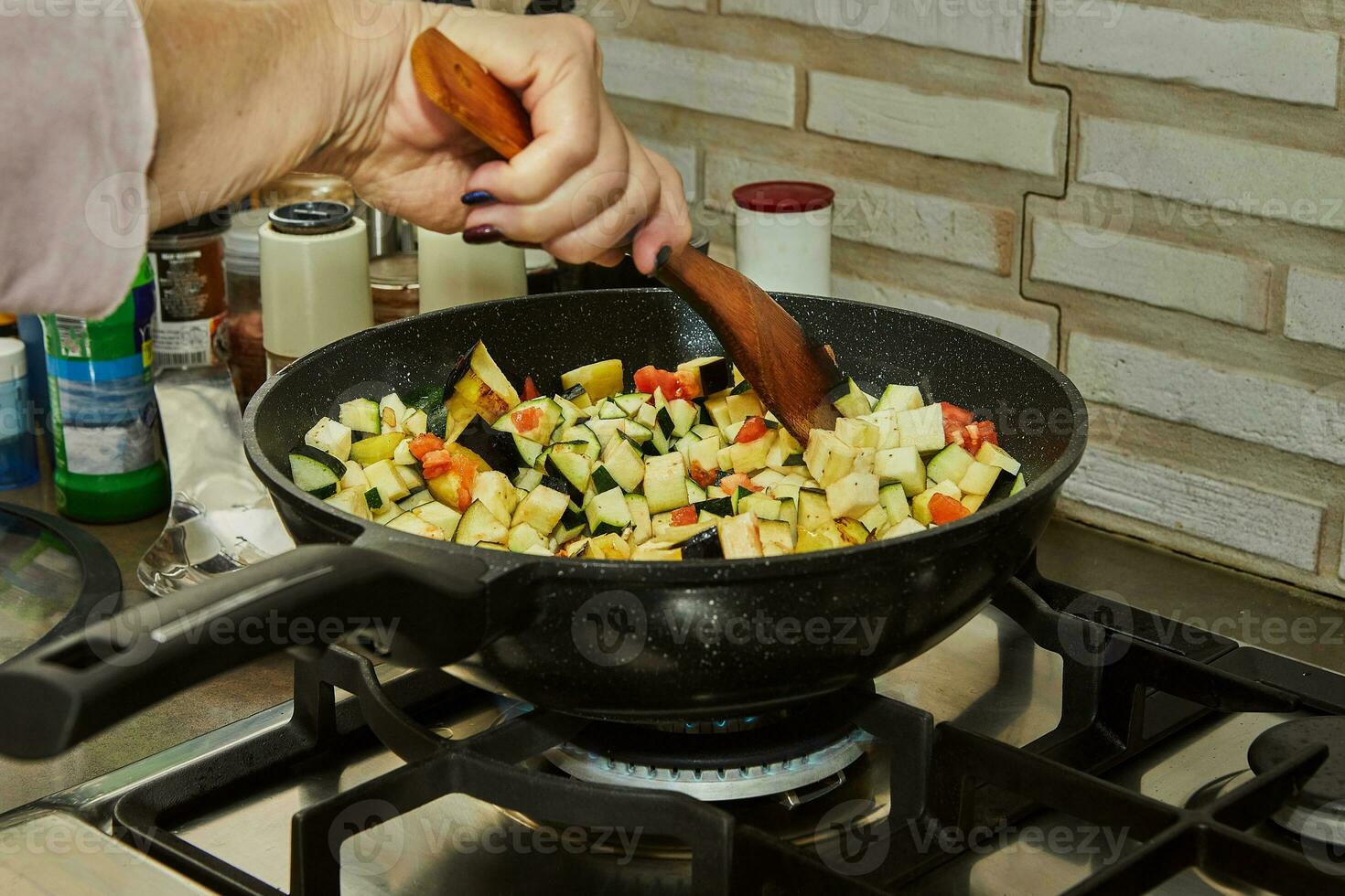 Chef stirs chopped tomatoes and eggplant into pot with ingredients on gas stove photo