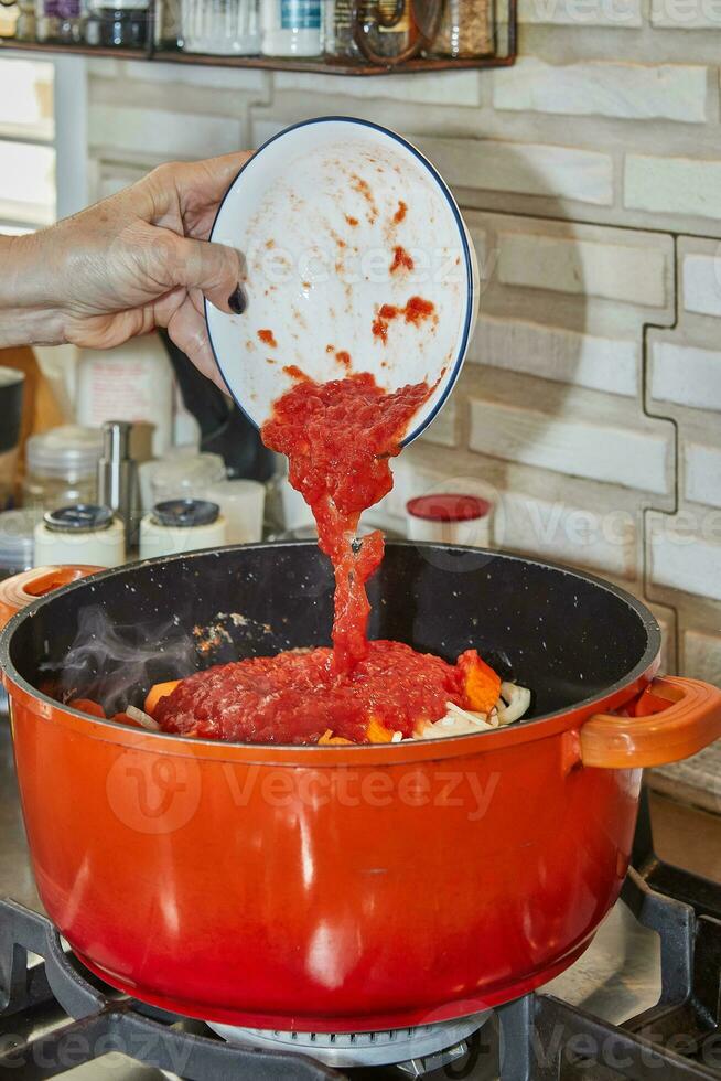 Chef adds tomato paste to the pot of ingredients on the gas stove photo