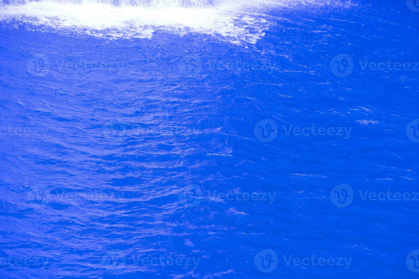 Blue water with ripples on the surface. Defocus blurred transparent blue colored clear calm water surface texture with splashes and bubbles. Water waves with shining pattern texture background. photo