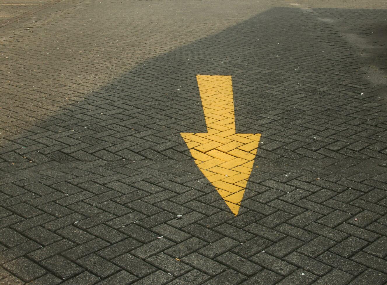 Yellow paint arrow symbol on brick ground public road street with small mini trash like paper and cigarettes on the road. photo