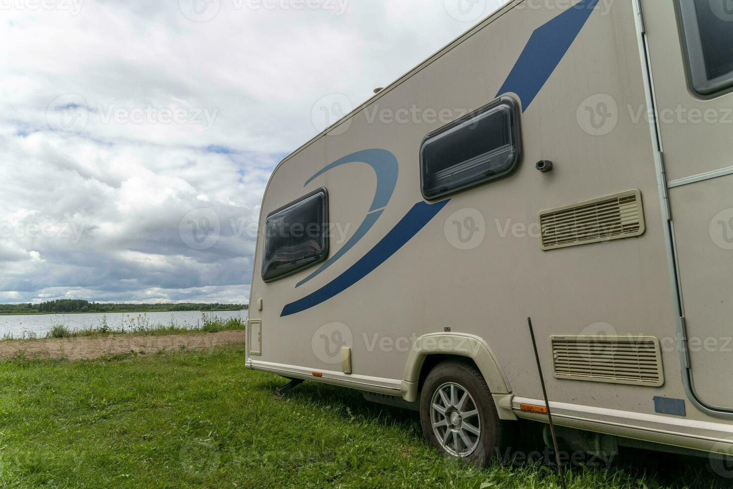 Camper trailer for traveling standing on shore of the lake in summer photo