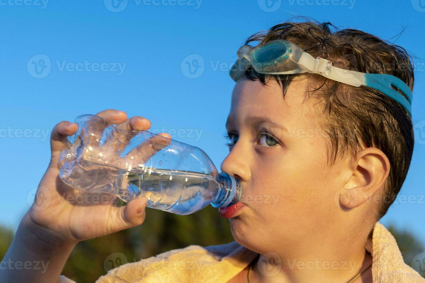 happy boy in swimming glasses drinks water from a bottle on the beach photo