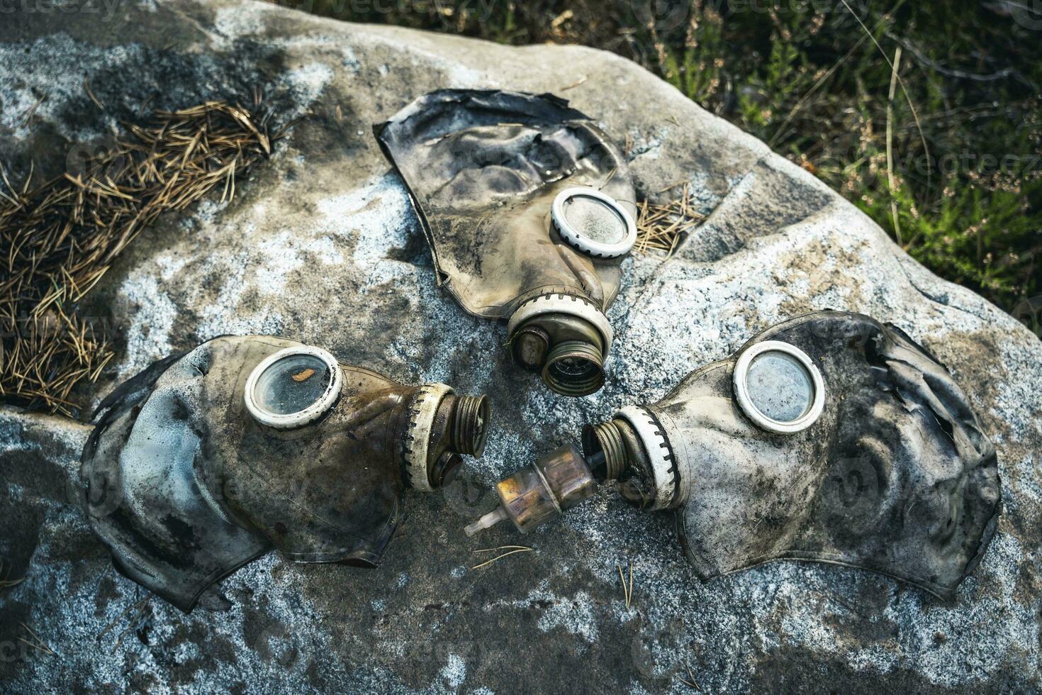 three old used gas masks are lying on a large boulder in the forest photo