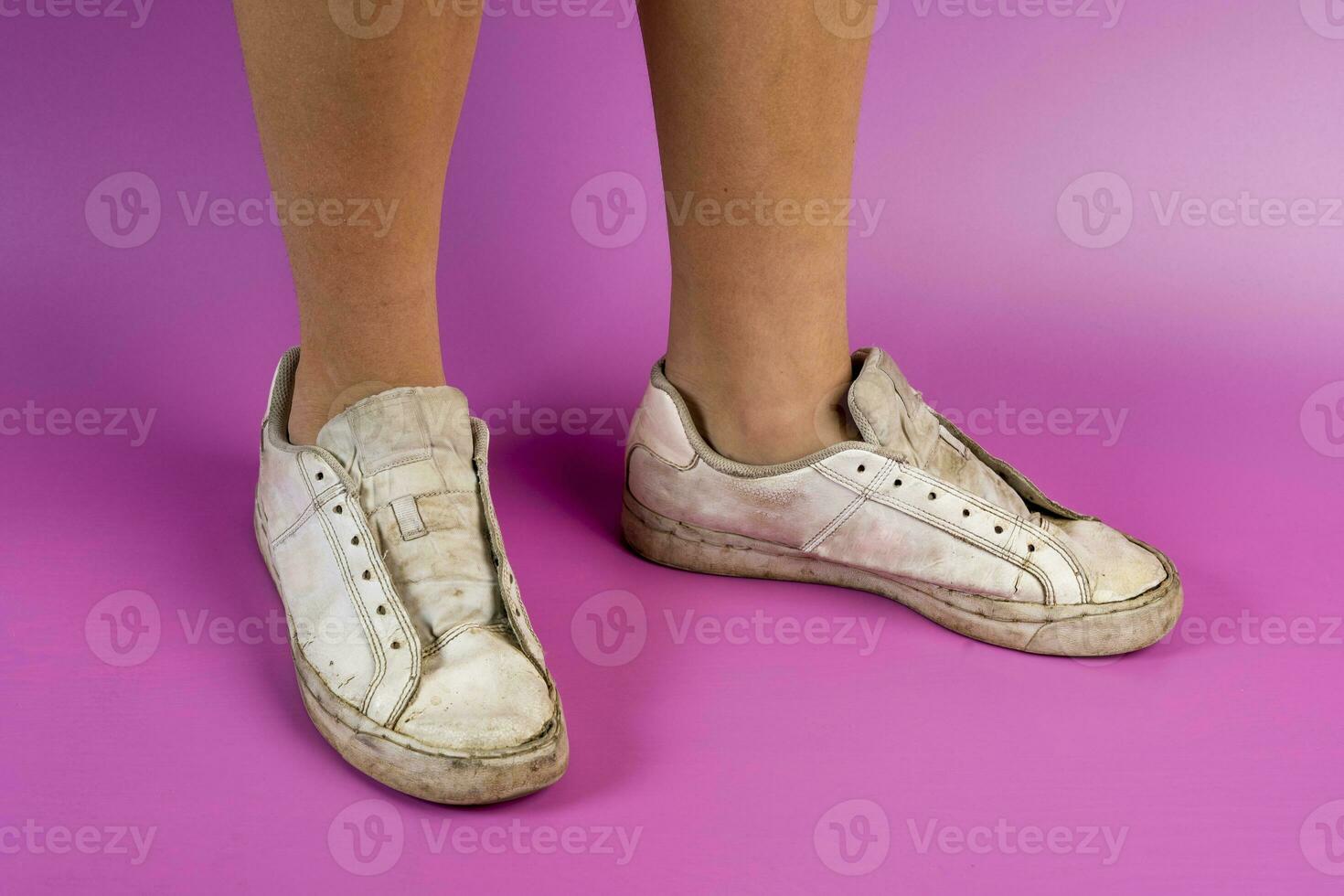 women's legs shod in old battered sneakers on a pink background photo